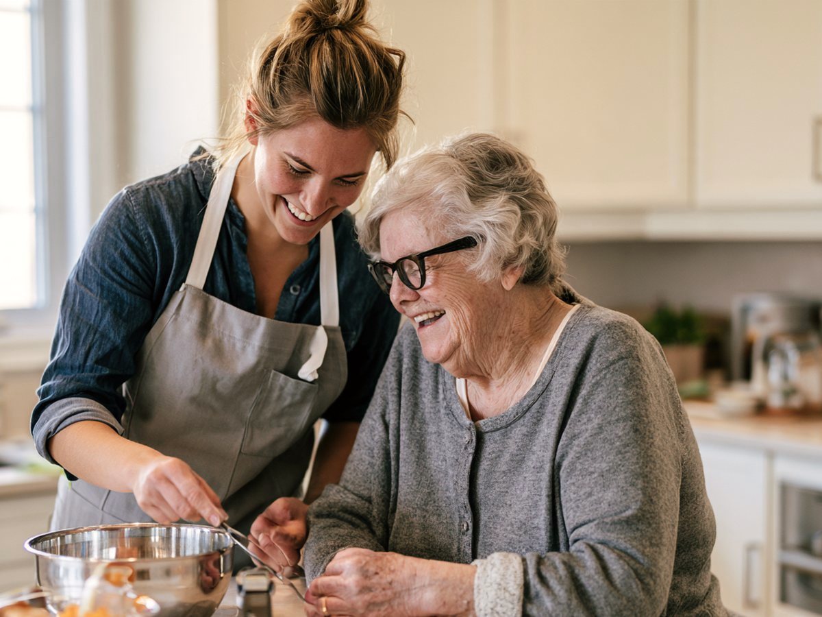 A senior and her companion laughing together while baking in a bright kitchen